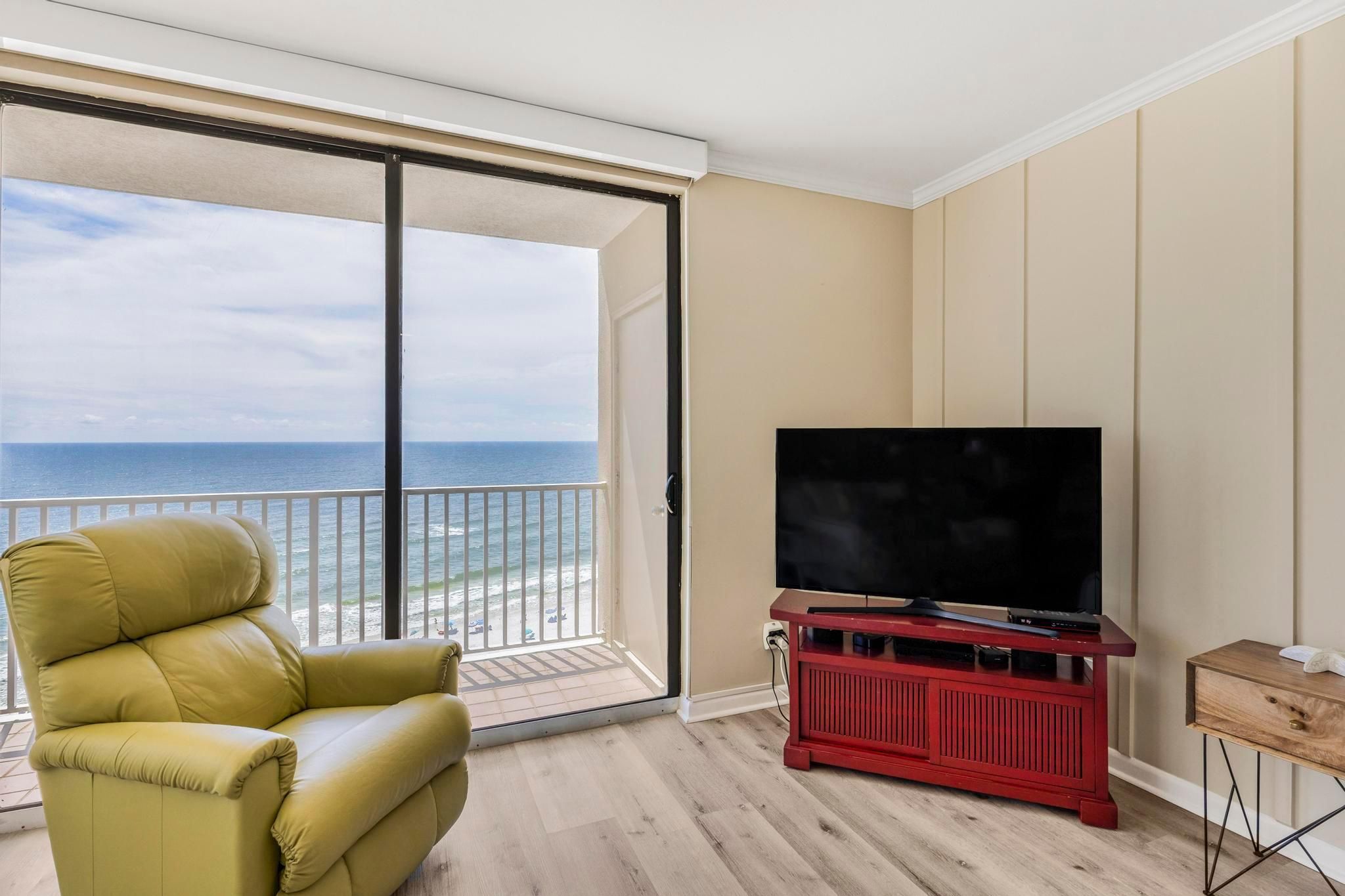 A balcony with a view of the ocean, a leather armchair, a red entertainment unit with a TV, and a wooden side table.