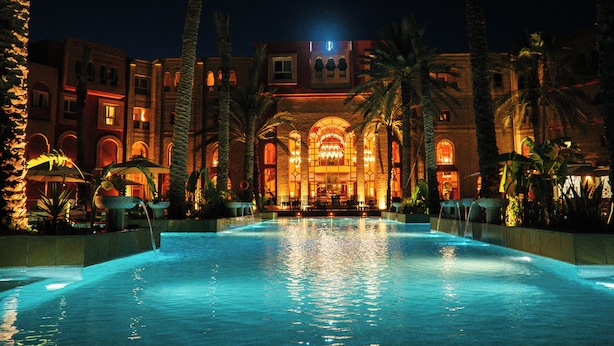 Ein Hotel mit Swimmingpool, Palmen und einem gut beleuchteten Eingangsbereich.
