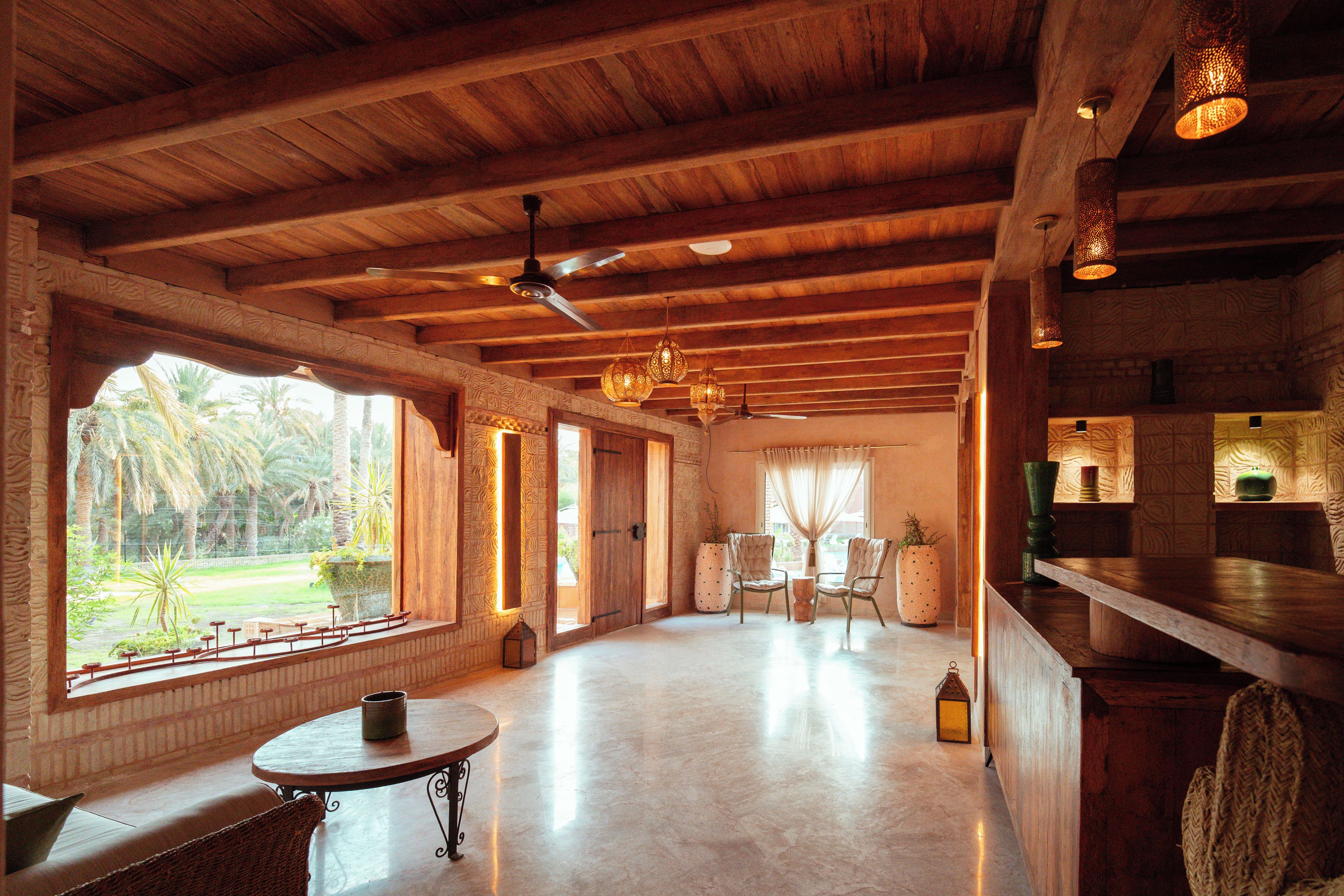 Una habitación amplia con techo alto, vigas de madera, zona de comedor con sillas y una mesa, y ventanas grandes que ofrecen vistas al exterior.