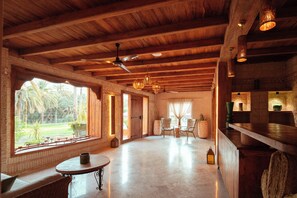 Una habitación amplia con techo alto, vigas de madera, zona de comedor con sillas y una mesa, y ventanas grandes que ofrecen vistas al exterior.