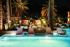 Zona junto a la piscina con sillones de descanso y palmeras de noche.