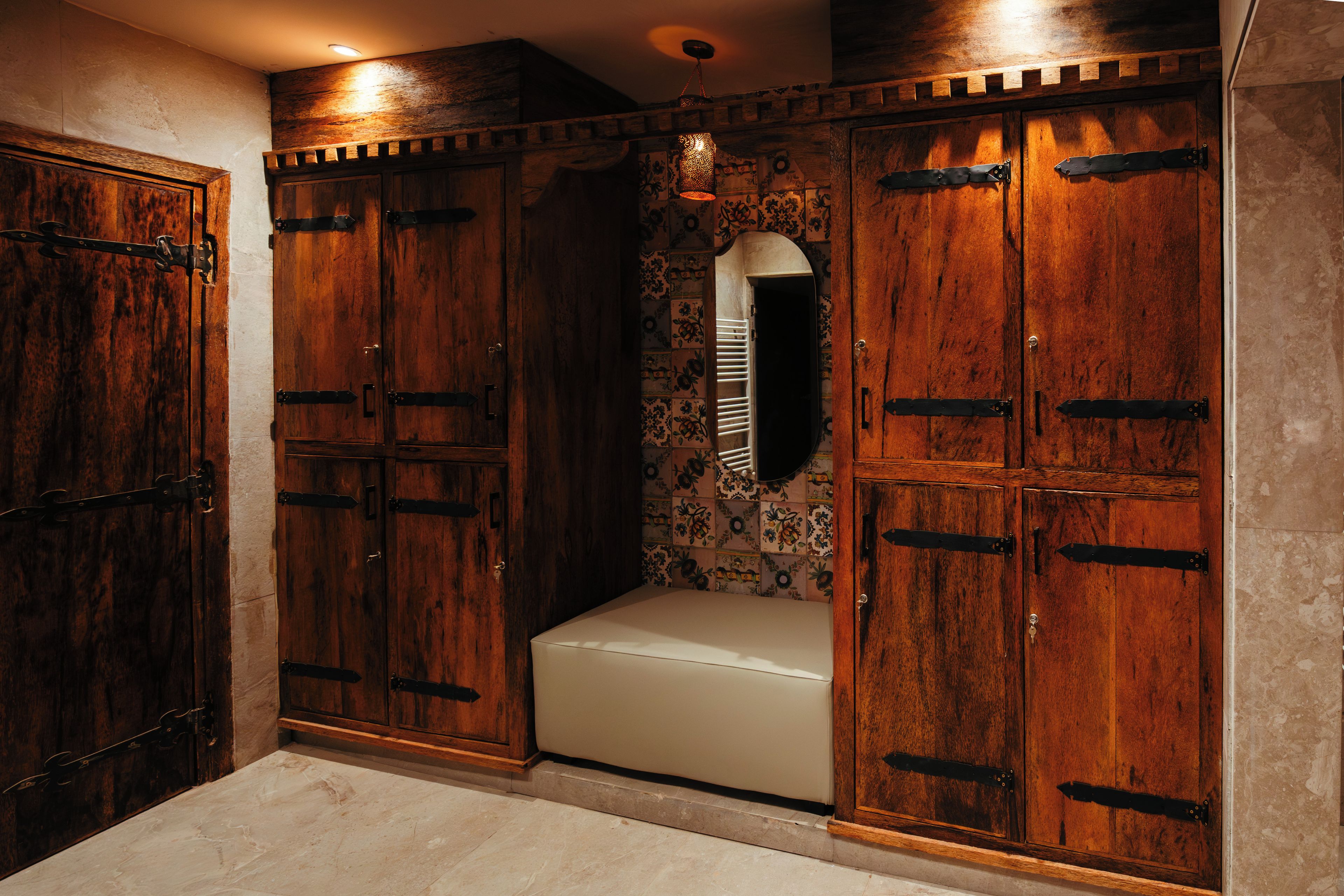 Una habitación con armarios de madera, un banco y un espejo decorativo.