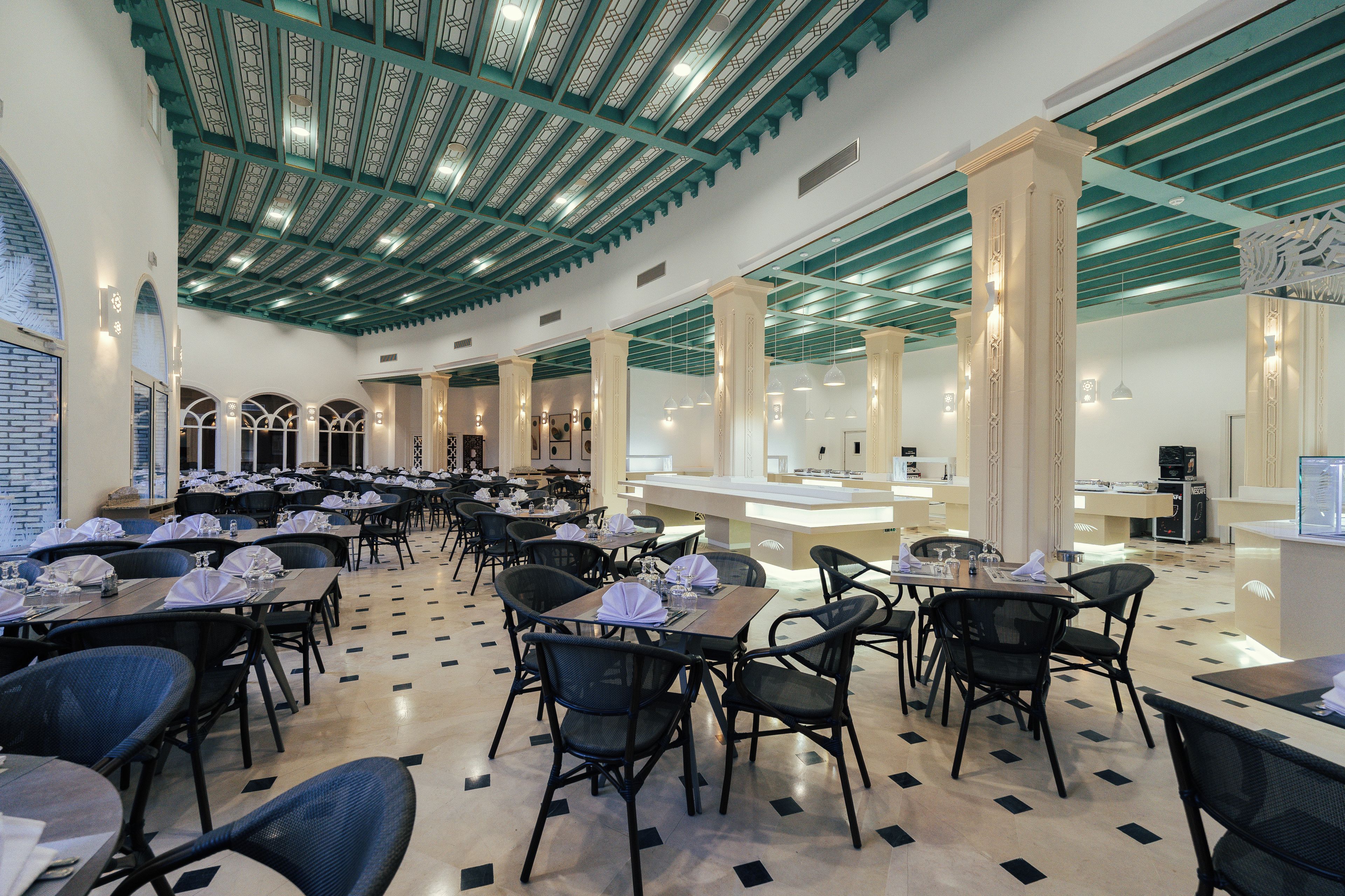 Un restaurant spacieux avec de hauts plafonds, un éclairage moderne et une disposition propre et bien organisée.