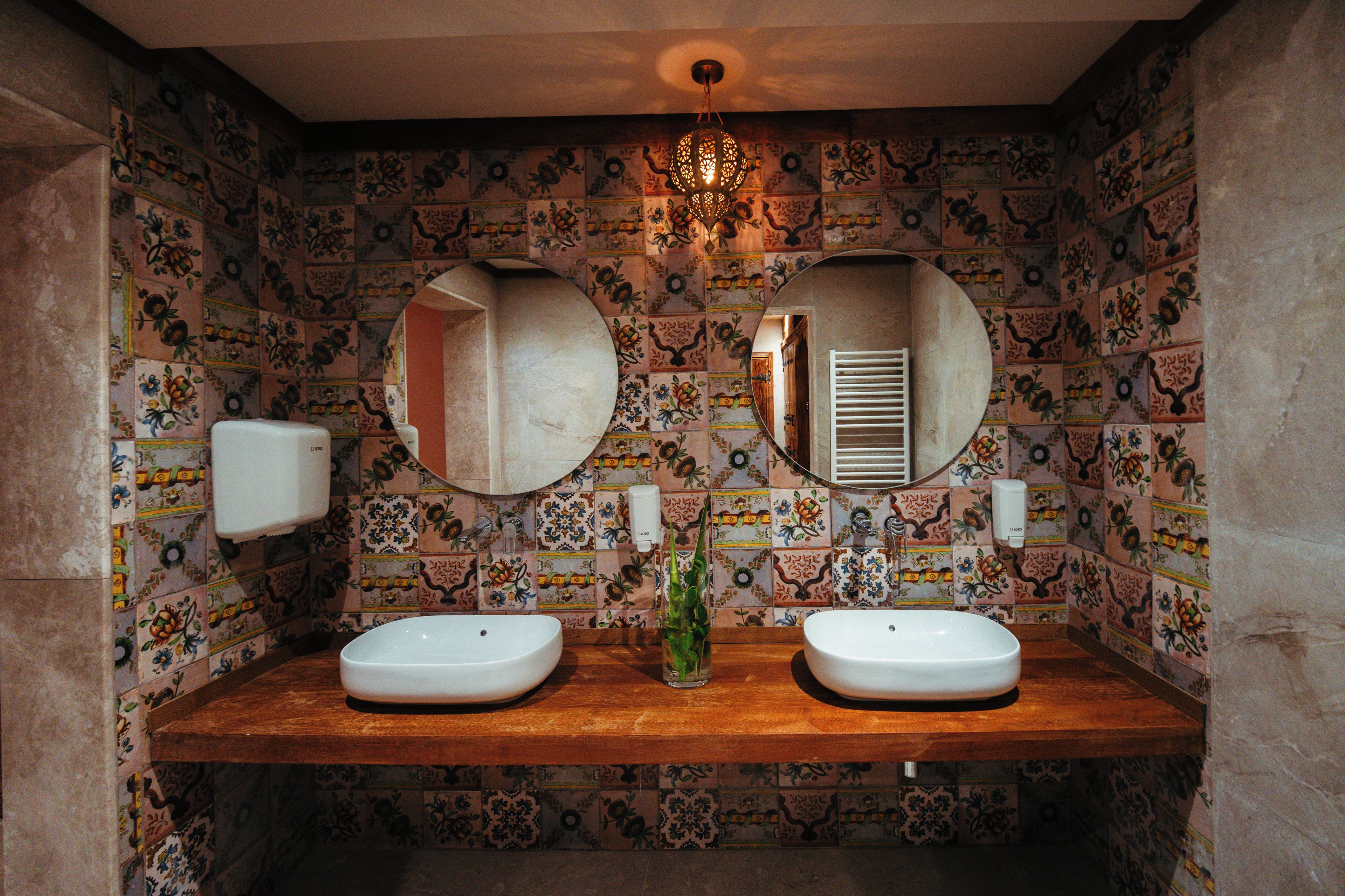 A bathroom with two sinks, a mirror, a chandelier, and decorative tiles.