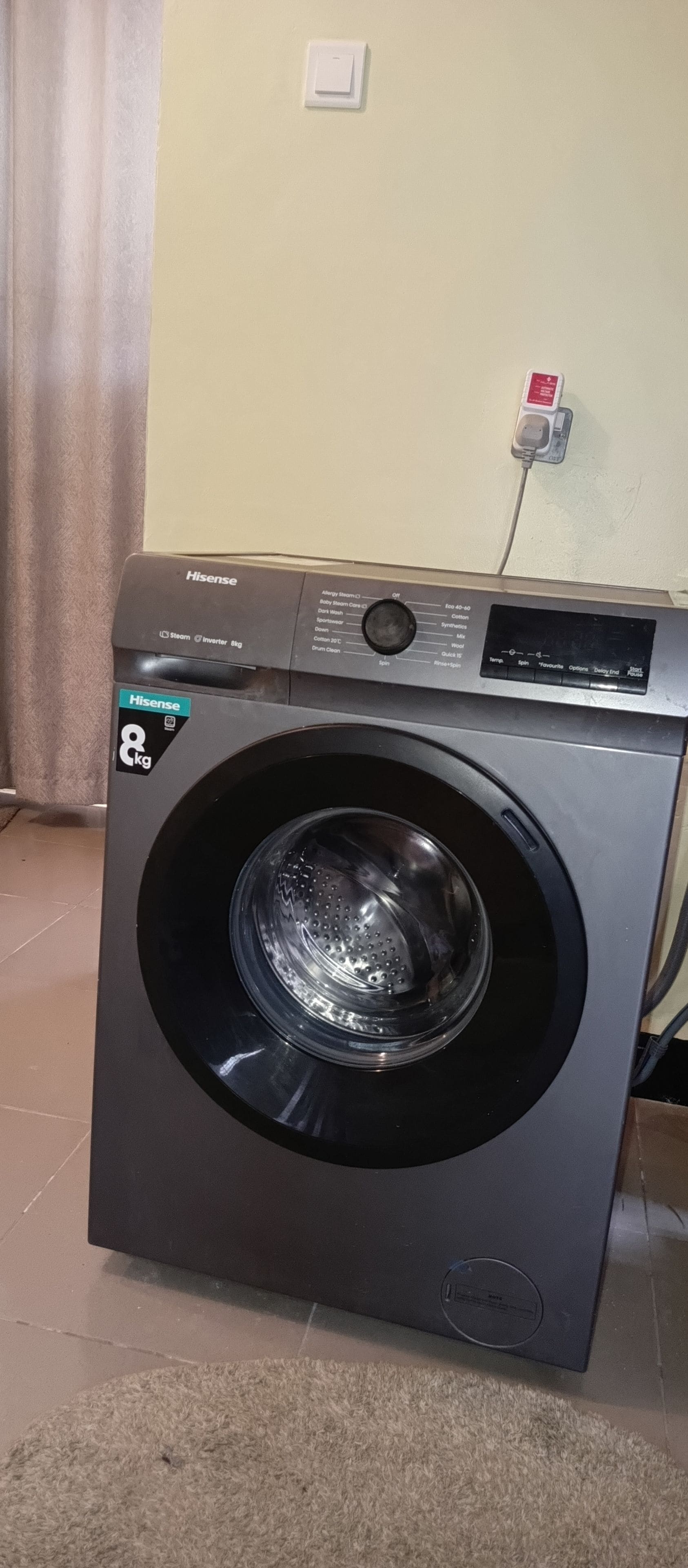 A front-loading Hisense 8kg front-loading washing machine with a control panel, located in a room with a tiled floor and a curtain.