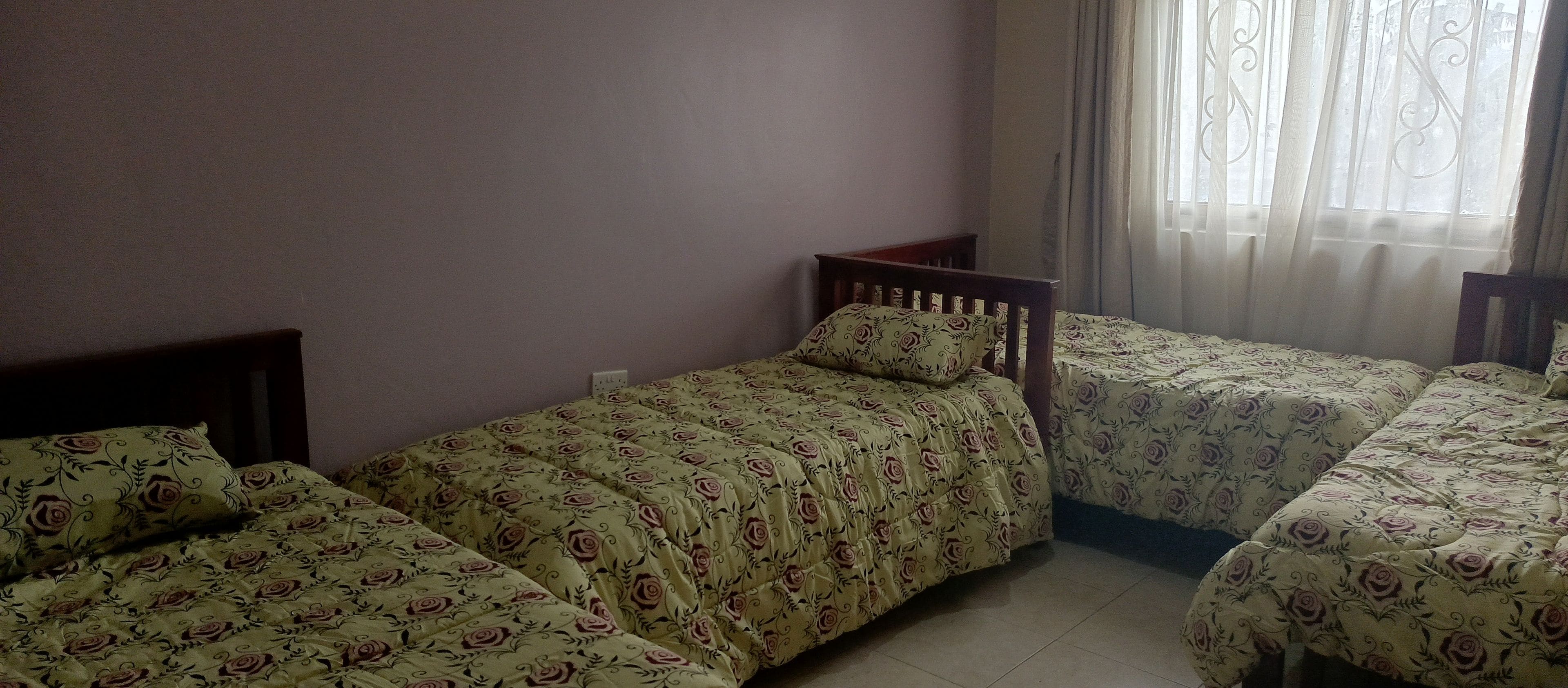Une chambre avec deux lits simples, chacun agrémenté d’une couvre-lit à motifs floraux, d’une tête de lit en bois et d’une fenêtre ornée de rideaux légers.