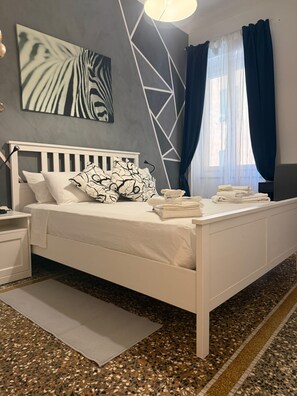 A modern bedroom with a white bed, a nightstand, a bedside table, a wall art piece, a geometric light fixture, and a window with curtains. - Spacious 4-bedroom apartment in delightful Genova with AC (Genova)
