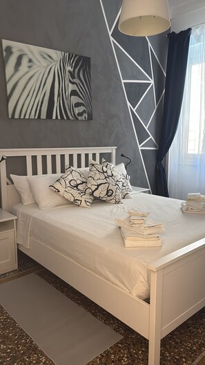 A neatly made bed with pillows, a bedside table, a lamp, and a window with curtains. - Spacious 4-bedroom apartment in delightful Genova with AC (Genova)