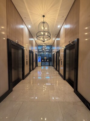 A hotel lobby with a polished marble floor, modern elevator doors, and a central chandelier. - New! Roomy & Zen Wi-fi 350Mbps  Uptown BGC, One Uptown Residence (Taguig)