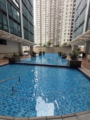 An indoor swimming pool with tiled flooring, surrounded by lounge chairs and potted plants. - New! Roomy & Zen Wi-fi 350Mbps  Uptown BGC, One Uptown Residence (Taguig)
