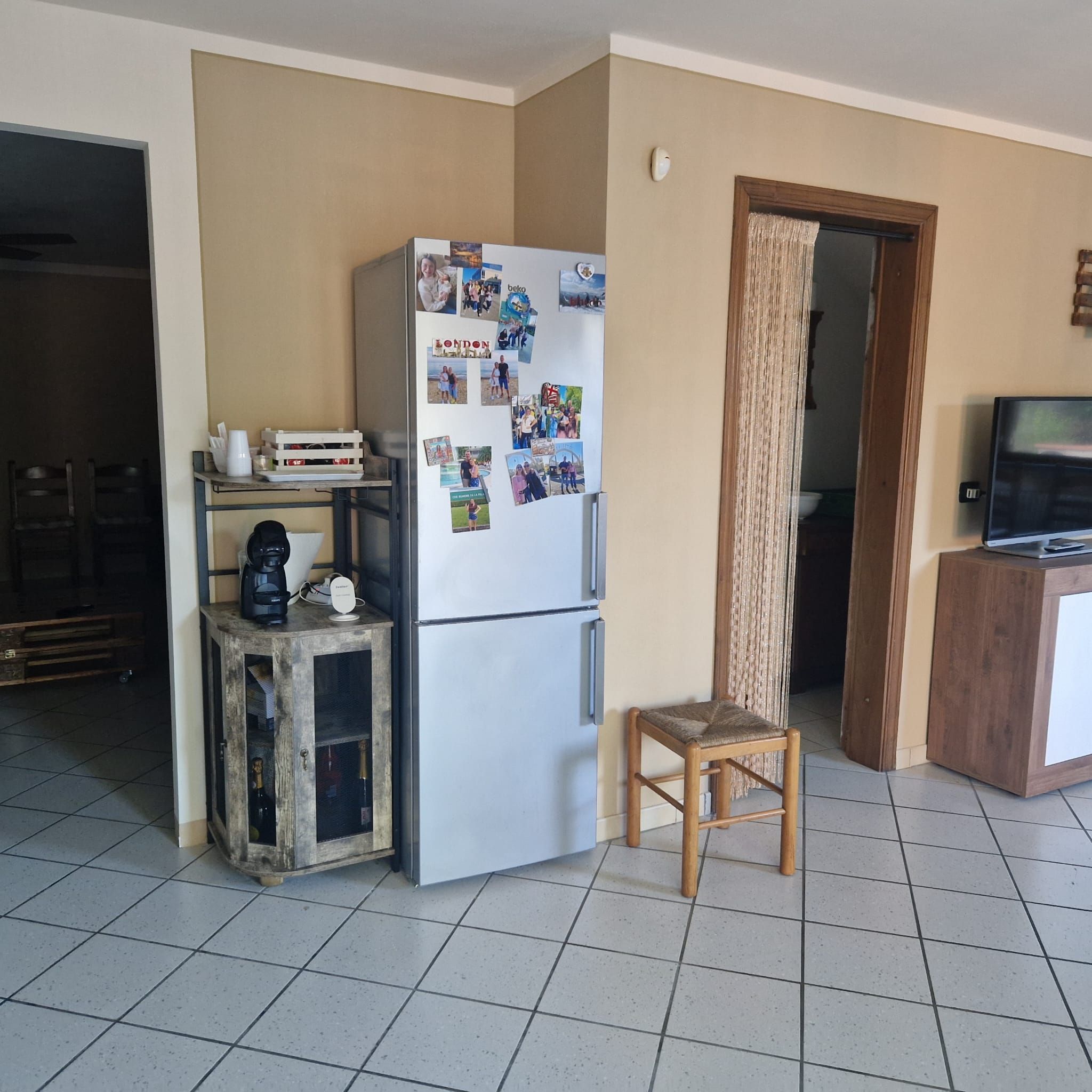 A compact kitchen with a refrigerator, a coffee machine, and a small wooden stool.