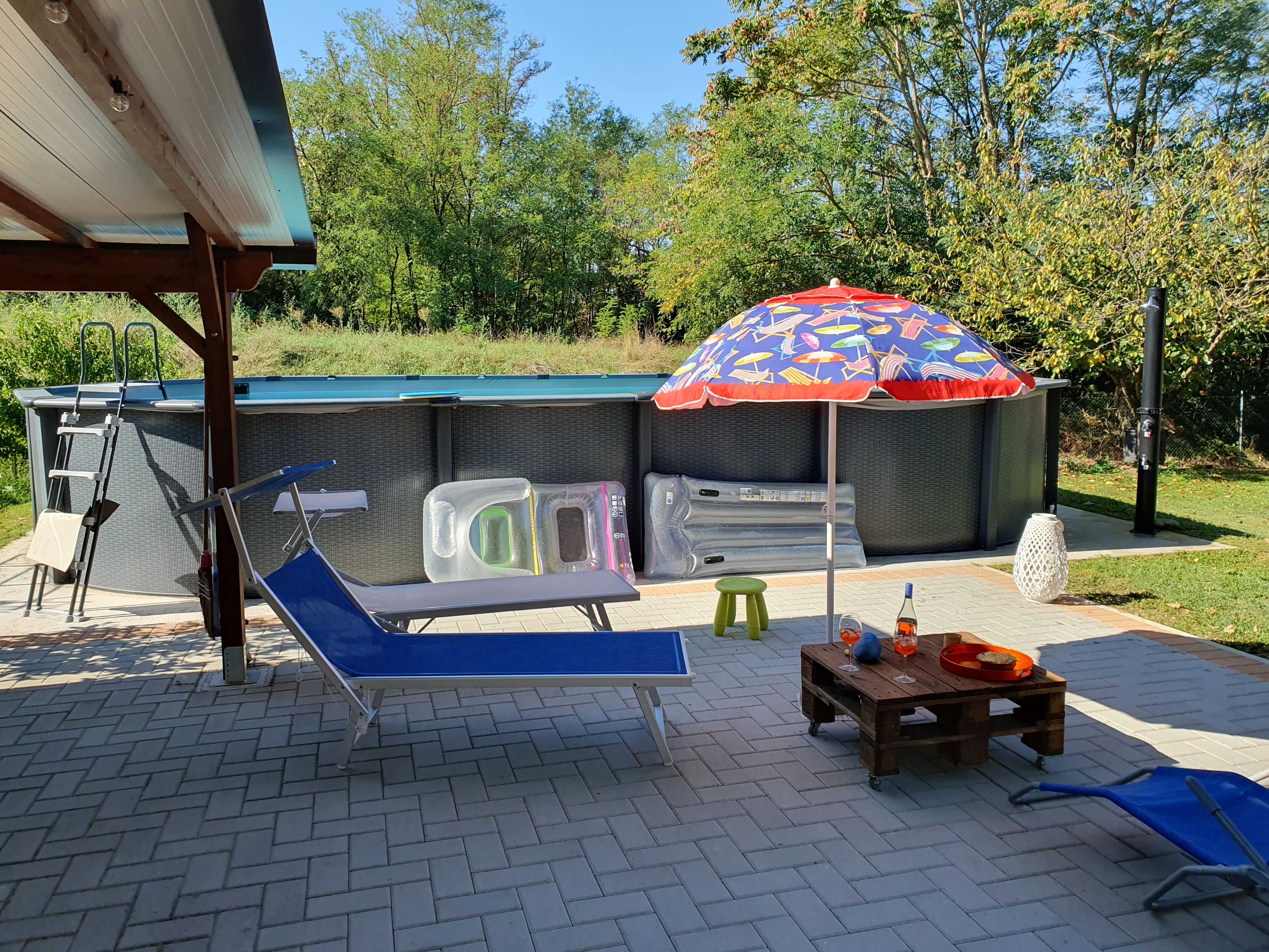 Een zwembadgedeelte met een ligbed, een klein tafeltje met drankjes en een kleurrijke parasol.