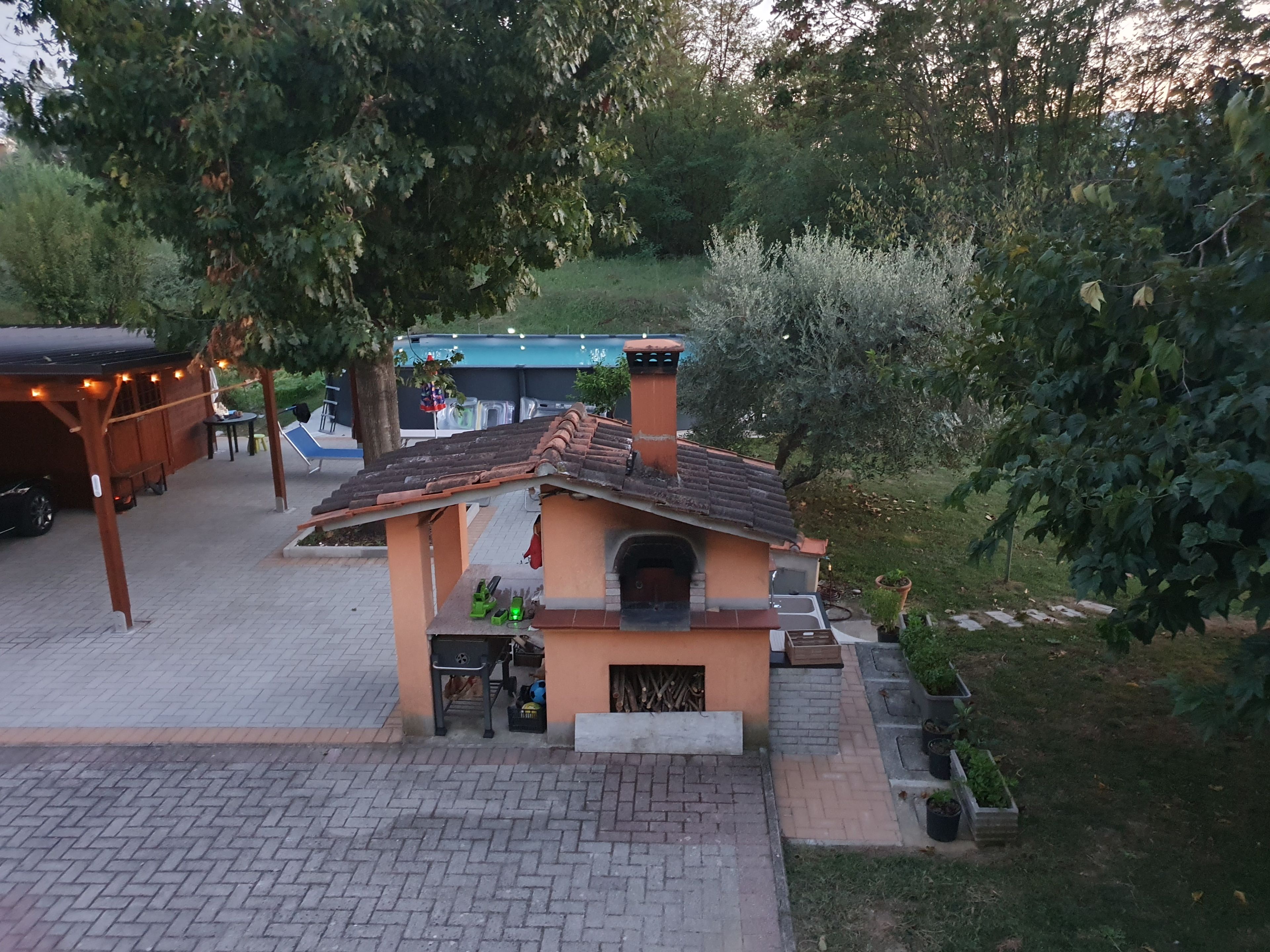 Une petite construction extérieure dotée d’un toit en tuiles, peut-être un espace barbecue, entourée de verdure et agrémentée d’une terrasse dallée.