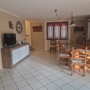 Een woonkamer met een televisie, houten meubels, een klok en een raam met jaloezieën.