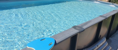 A swimming pool with a dark-colored deck and a blue safety rail.