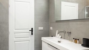 Een moderne badkamer met een douchecabine van glas, een witte deur en een witte wastafel met toiletartikelen.