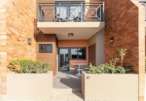 A modern apartment with a balcony, a small patio area with a table and chairs, and a number '10' on the wall. - LUX 1BR House Pool Gym 7-Min Walk Palm Beach - Porta Al Sole 8 by Bocobay (Noord)