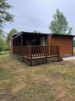 Eine kleine Holzhütte mit Veranda und Tür, umgeben von Gras und Bäumen.