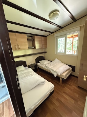 Ein gemütliches Schlafzimmer mit zwei Betten, Holzschränken, einem kleinen Fenster und einer Deckenleuchte.