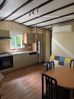 A kitchen with a built-in stove, a sink, and a window. There is a dining table with chairs and a bench with a cushion.