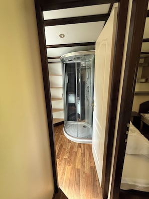 Ein Zimmer mit Holzboden, einer Glaskabine für die Dusche und einer weißen Tür.