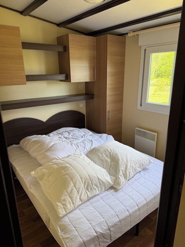 Ein Schlafzimmer mit einem Bett, Holzschränken, einem Fenster und einer fest eingebauten Heizung.