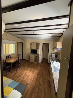 A compact kitchen with a dining area, wooden flooring, and built-in appliances.