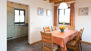 Un comedor con una mesa dispuesta para cuatro personas, sillas de madera, un frutero y una ventana con cortinas.