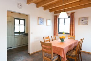 Un coin repas avec une table dressée pour quatre personnes, des chaises en bois, un saladier rempli de fruits et une fenêtre avec des rideaux.