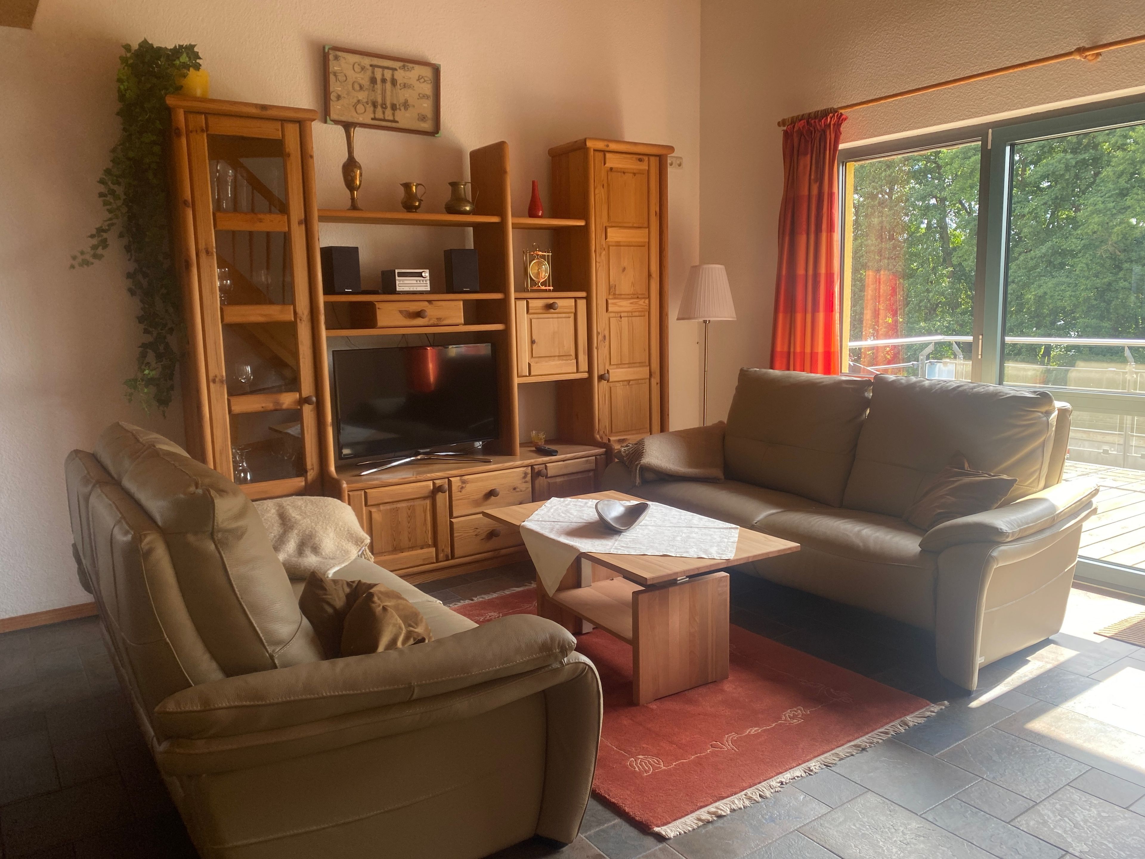 Ein Wohnzimmer mit einer Couch, einem Fernseher, Holzschränken und einem Fenster mit Vorhängen.