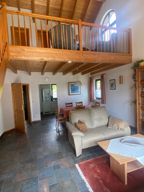 Un vaste espace de vie doté d’un haut plafond en bois, d’une table à manger, d’un canapé et d’un escalier menant à un niveau supérieur.