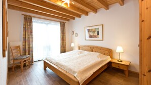Un dormitorio con una cama de madera, dos lámparas de noche, una silla y una ventana con cortinas.
