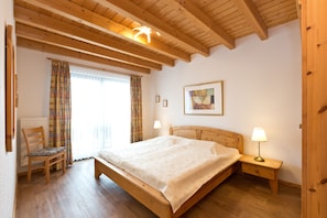Une chambre à coucher avec un lit en bois, deux lampes de chevet, une chaise et une fenêtre avec des rideaux.