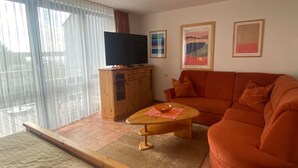 Una sala de estar con un sofá, un televisor sobre un mueble de madera y una ventana con persianas.