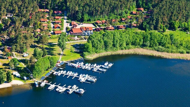 Vista aérea de una propiedad junto al lago con un puerto deportivo, casas y un bosque denso.