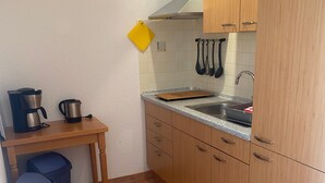 Una cocina compacta con lavamanos, armarios de madera, una encimera y una pequeña mesa con cafetera.