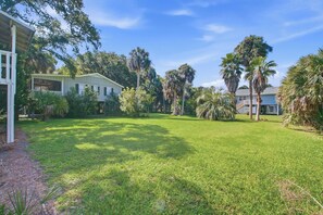 A residential property with a well-maintained lawn, multiple palm trees, and a two-story house with a balcony. - Edisto Escape (Edisto Island)
