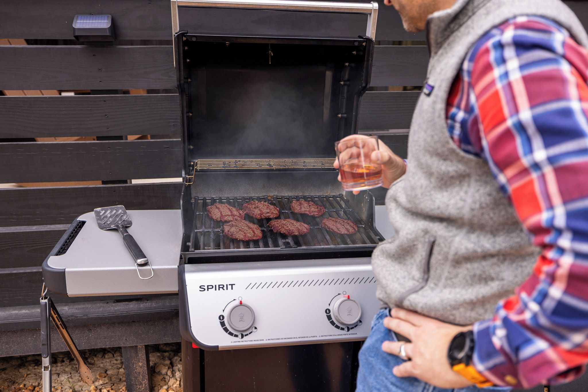 A person grilling hamburgers on an outdoor grill with a control panel labeled 'SPIRIT'.