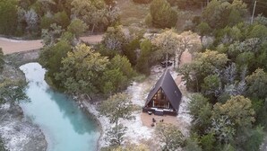 A cabin surrounded by trees and a body of water. - A quiet A-frame escape in the Texas countryside, made for slowing down. (Ledbetter)
