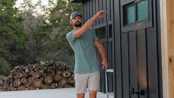 A person standing next to a building with a door, a pile of logs, and a wooden board on the ground.