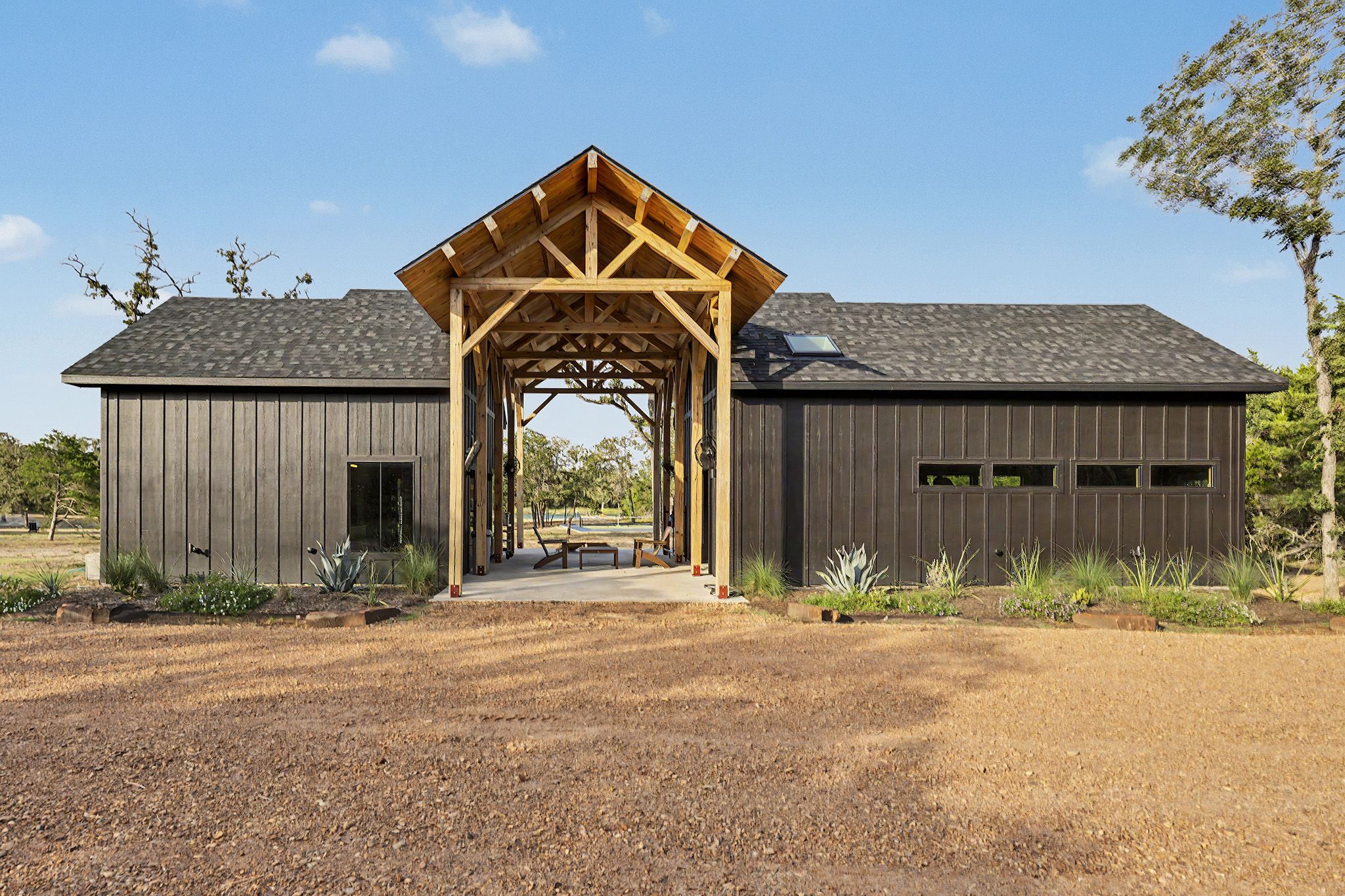 A rustic barn with a covered entryway, open garage doors, and a gravel driveway.