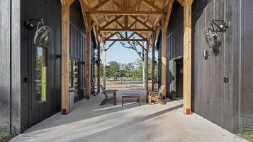 A covered outdoor area with a concrete floor, wooden benches, and a view of a park with trees and a clear sky.