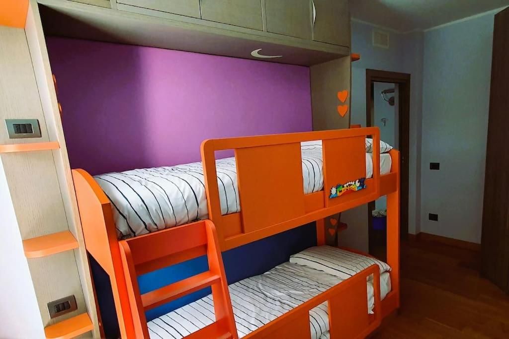 Un letto a castello con ringhiere arancioni e biancheria a righe, una parete viola e una porta decorata con un cuore.