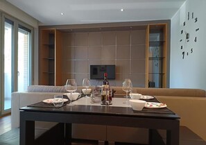 A modern living room with a sofa, a dining table set for four, and a television mounted on the wall. - As cozy as your own home!  Comfort and genuine hospitality in the heart of Ravenna. (Ravenna)