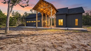 A modern building with a covered patio area, large windows, and a flat roof. - A quiet A-frame escape in the Texas countryside, made for slowing down. (Ledbetter)