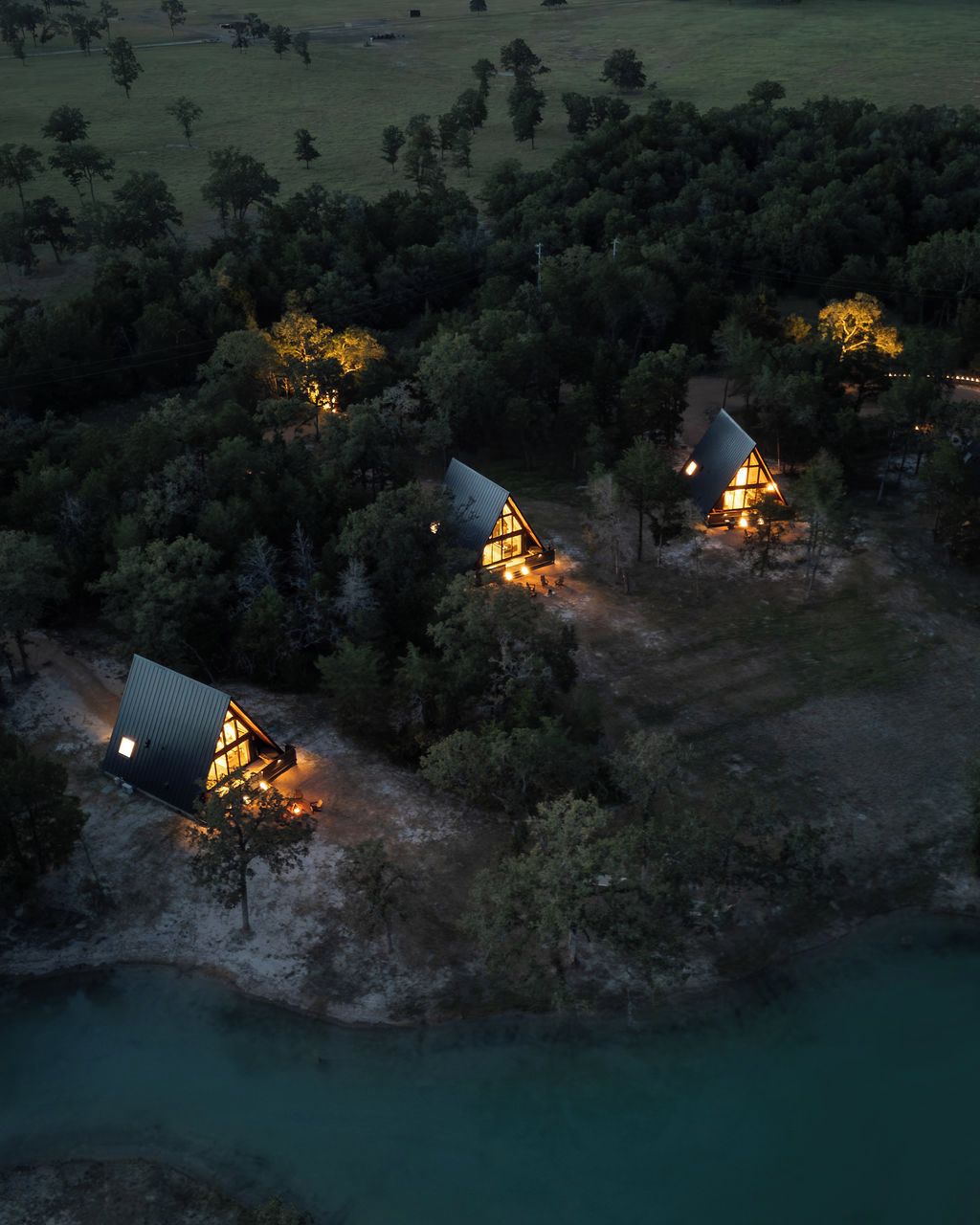 Zona apartada de cabañas con tres alojamientos rodeados de bosque denso, accesible por un sendero de tierra.