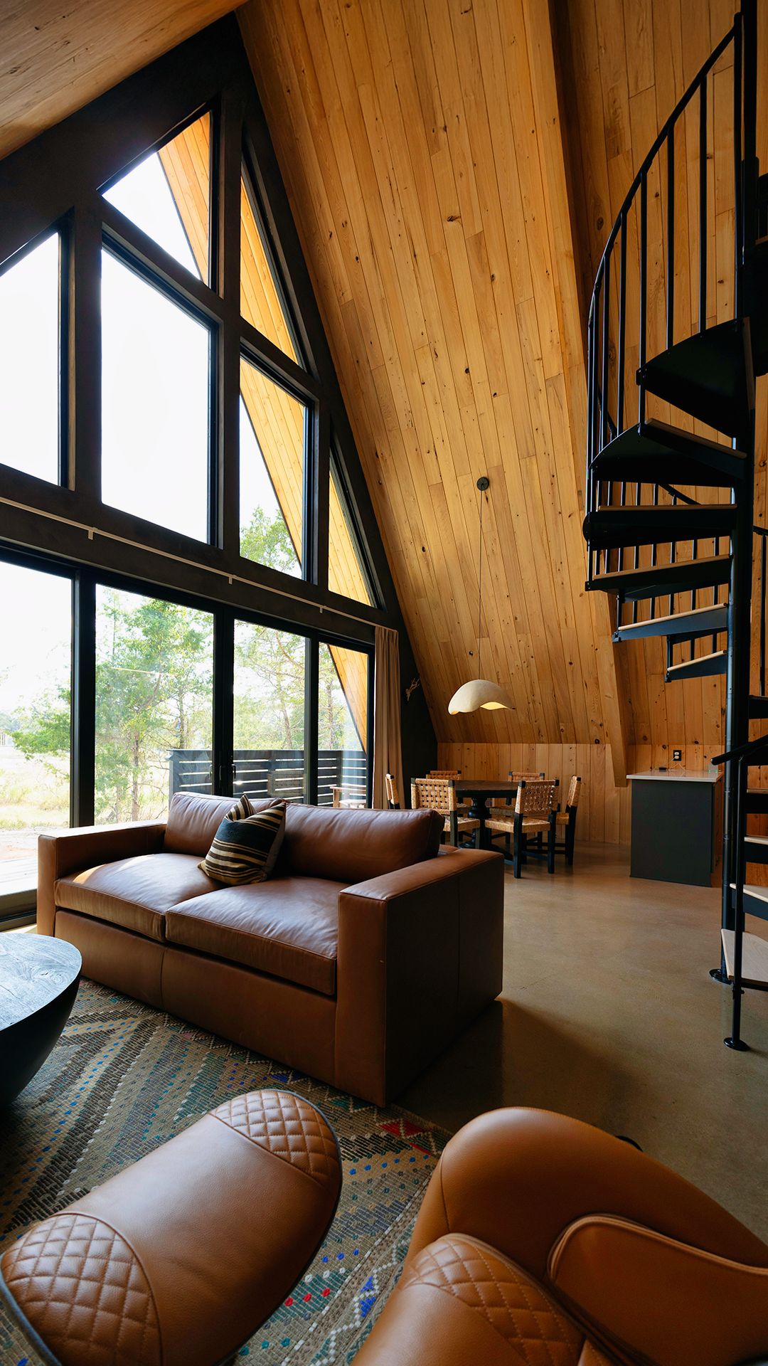 Ein geräumiges Loft mit hoher Decke, einer geschwungenen Treppe, einer Ledersofa und einem Essbereich mit viel Tageslicht durch große Fenster.
