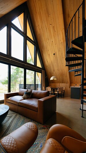 A spacious loft with a high ceiling, a curved staircase, a leather sofa, and a dining area with natural light from large windows.