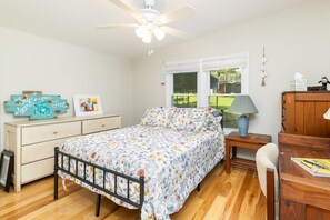 Ein Schlafzimmer mit Bett, Schminktisch, Nachttisch, Lampe und Blick ins Freie durch ein Fenster.