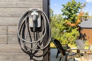 Una estació de càrrega per a vehicles elèctrics fixada a la paret, amb un cable, un mur de fusta i seients a l'aire lliure.